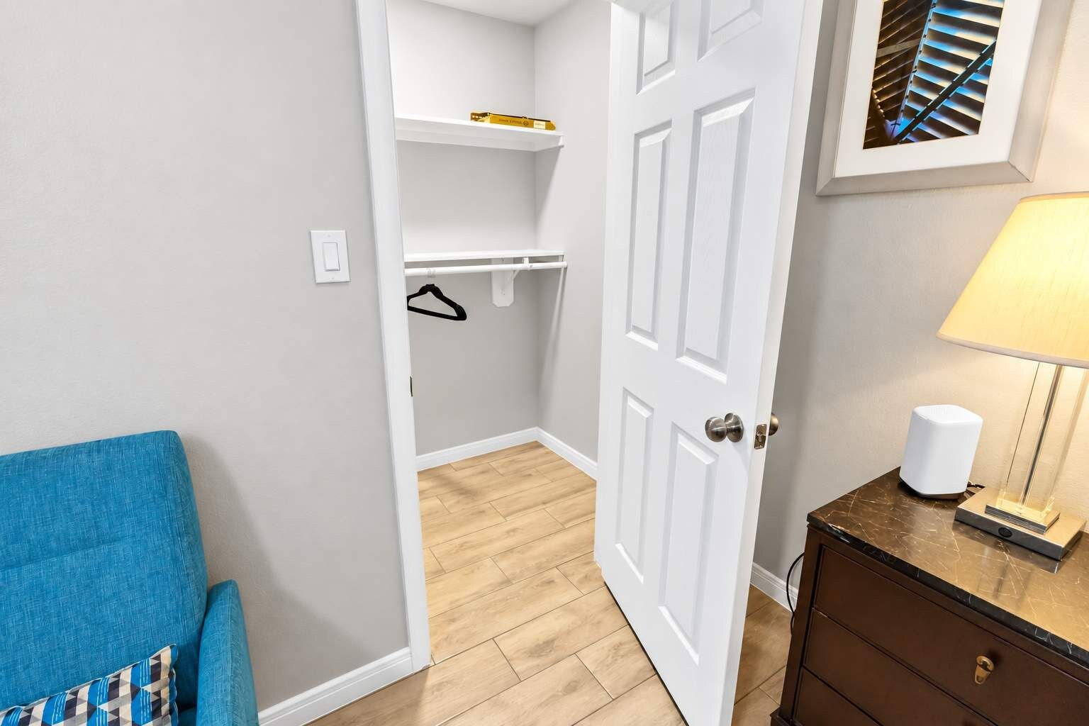 A room with a blue sofa, a wooden cabinet, a white door, and a wall-mounted shelf.