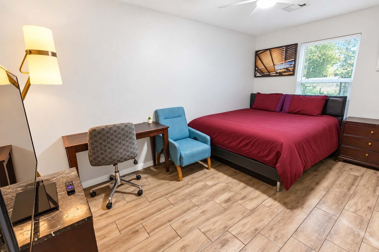 Ein Schlafzimmer mit einem Bett, einem Schreibtisch, einem Stuhl, einer Kommode und einer Lampe.