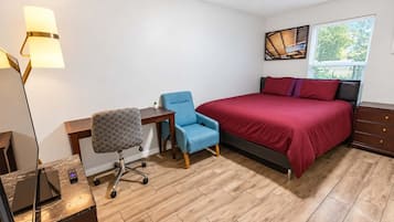 Ein Schlafzimmer mit einem Bett, einem Schreibtisch, einem Stuhl, einer Kommode und einer Lampe.