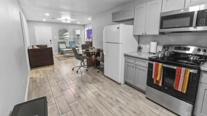 A modern kitchen with stainless steel appliances, a dining area with a table and chairs, and a hallway leading to a door. - 4BR Workspace Home | 2.5 Baths | Sleeps 8 (Houston)