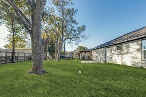 Un patio trasero residencial con un árbol grande, un césped y una casa con garaje.