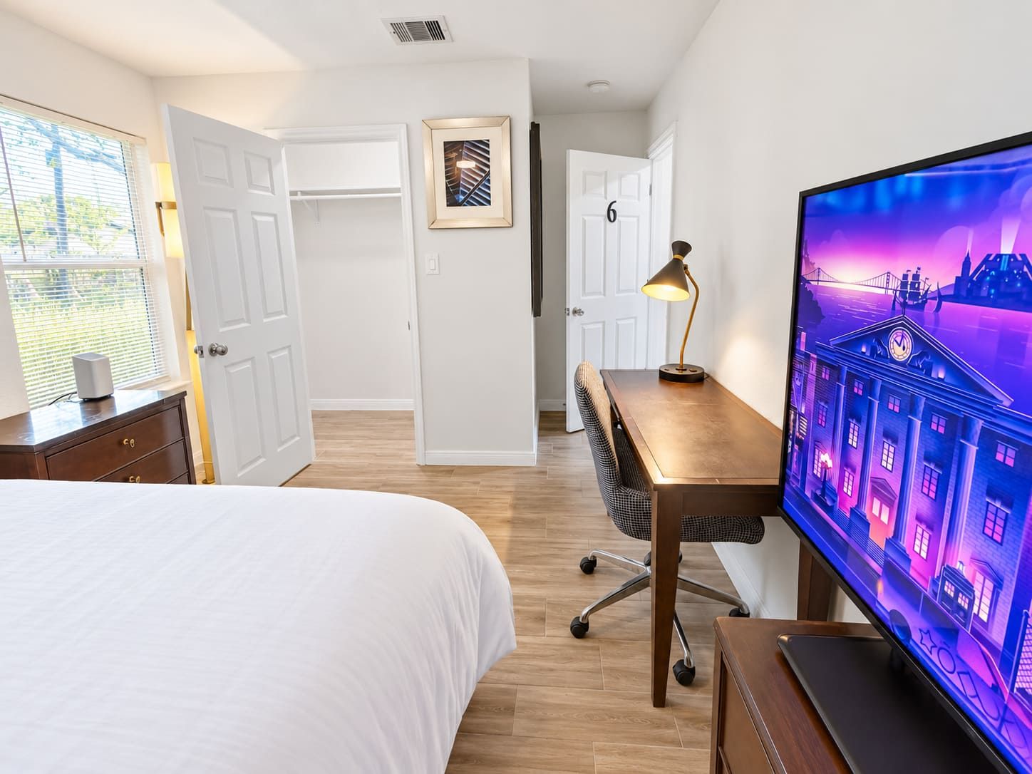 A hotel room with a bed, desk, chair, TV, and a door leading to another room.