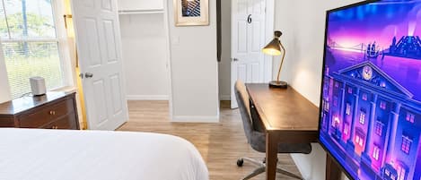 A hotel room with a bed, desk, chair, TV, and a door leading to another room.