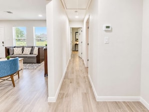 A modern interior with a hallway leading to a living area and kitchen. - 4BR Crew Home | 4 Desks, Driveway, Near Hobby (Houston)