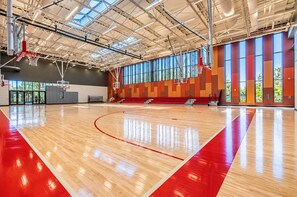 An indoor basketball court with a wooden floor, red lines, and a high ceiling with skylights.