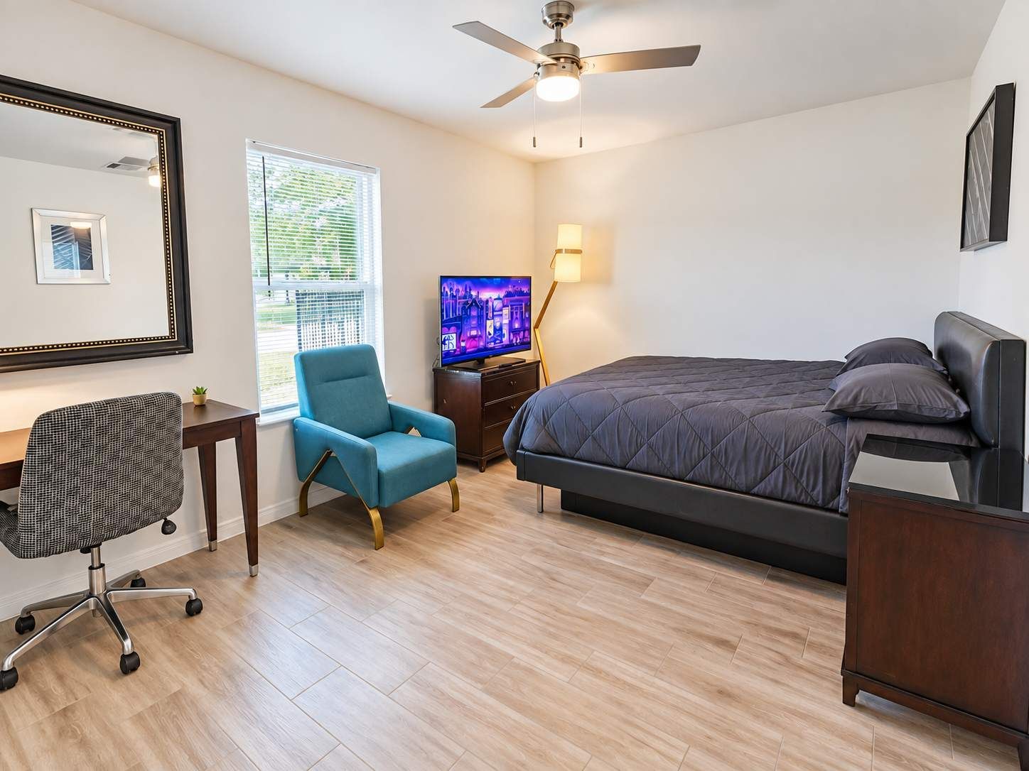 A bedroom with a bed, a desk, a chair, a TV, and a ceiling fan.