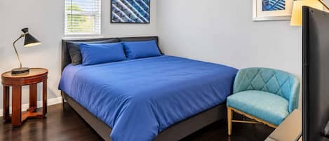 Ein Schlafzimmer mit einem Bett, einem Sessel, einer Lampe und zwei gerahmten Bildern an der Wand.