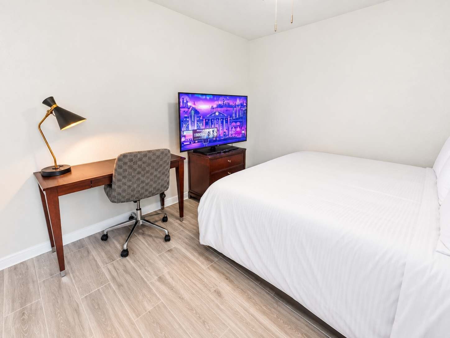A hotel room with a bed, a desk with a chair, a television, and a lamp.