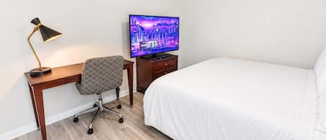 Une chambre d’hôtel comprenant un lit, un bureau avec une chaise, une télévision et une lampe.