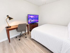 A hotel room with a bed, a desk with a chair, a television, and a lamp.