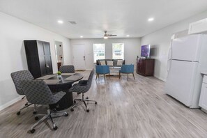 Una sala de estar moderna con una mesa de comedor, sillas, un sofá, un televisor y un refrigerador.