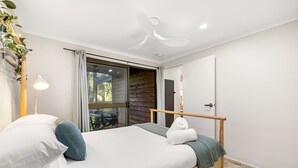 A bedroom with a bed, a bedside lamp, a ceiling fan, and a view through a glass door to an outdoor area.