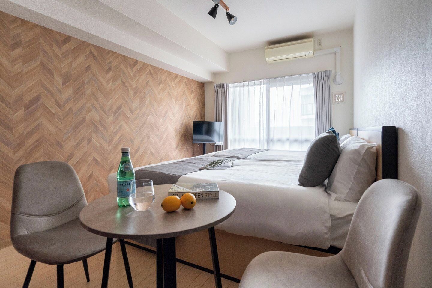 A hotel room with a bed, a desk with a chair, a bottle of water, and two oranges on the desk.