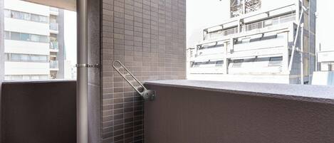 A balcony with a metal railing, a tiled wall, and a view of adjacent buildings.