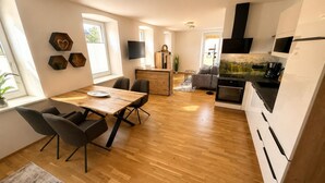 Une cuisine moderne dotée d’un four encastré, un coin repas avec une table et des chaises en bois, et un espace de vie comprenant un canapé et un téléviseur.