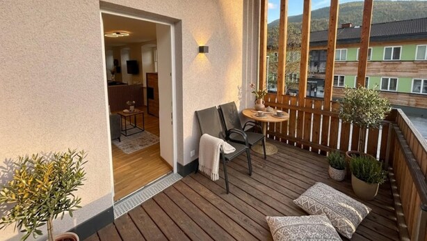 Un balcon doté d’un plancher en bois, un coin salon avec une table et des chaises, et des plantes en pot.