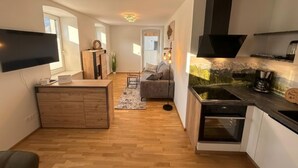 Une cuisine compacte dotée d’un four encastré, un coin repas avec un canapé et un téléviseur fixé au mur.