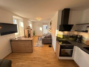Eine kompakte Küche mit integriertem Backofen, ein Essbereich mit einer Couch und einem an der Wand montierten Fernseher.