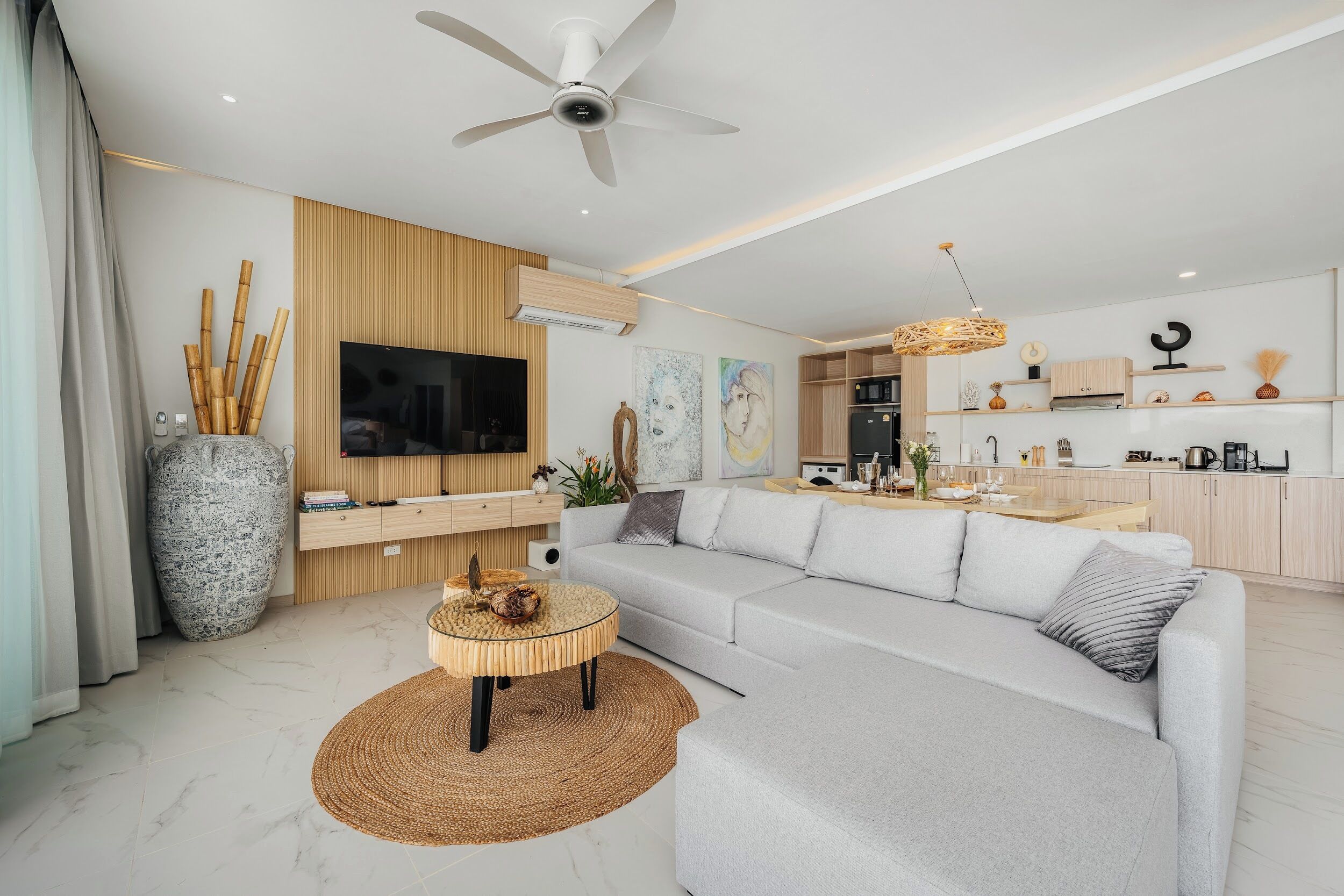 A modern living room with a sofa, a TV, a ceiling fan, and a kitchen area with cabinets and a dining table.