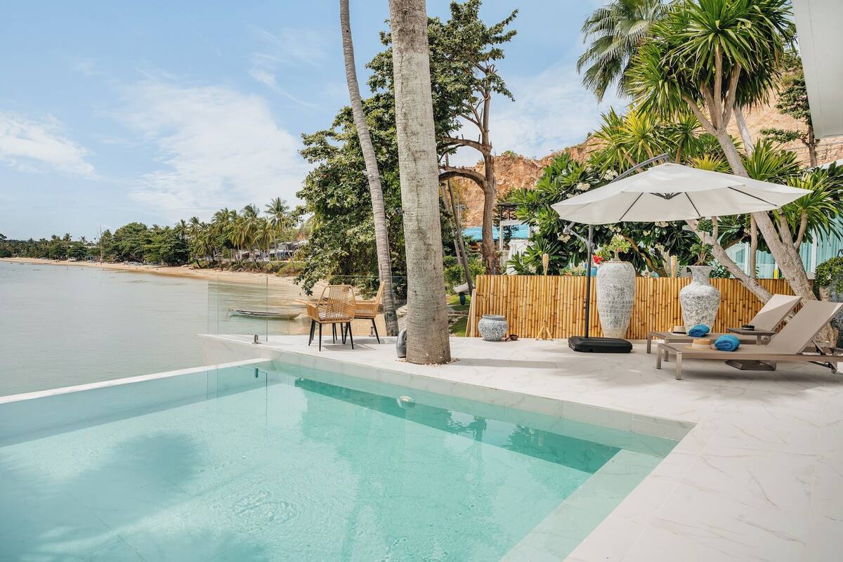 A pool area with a view of the beach, lounge chairs, and a bamboo fence.