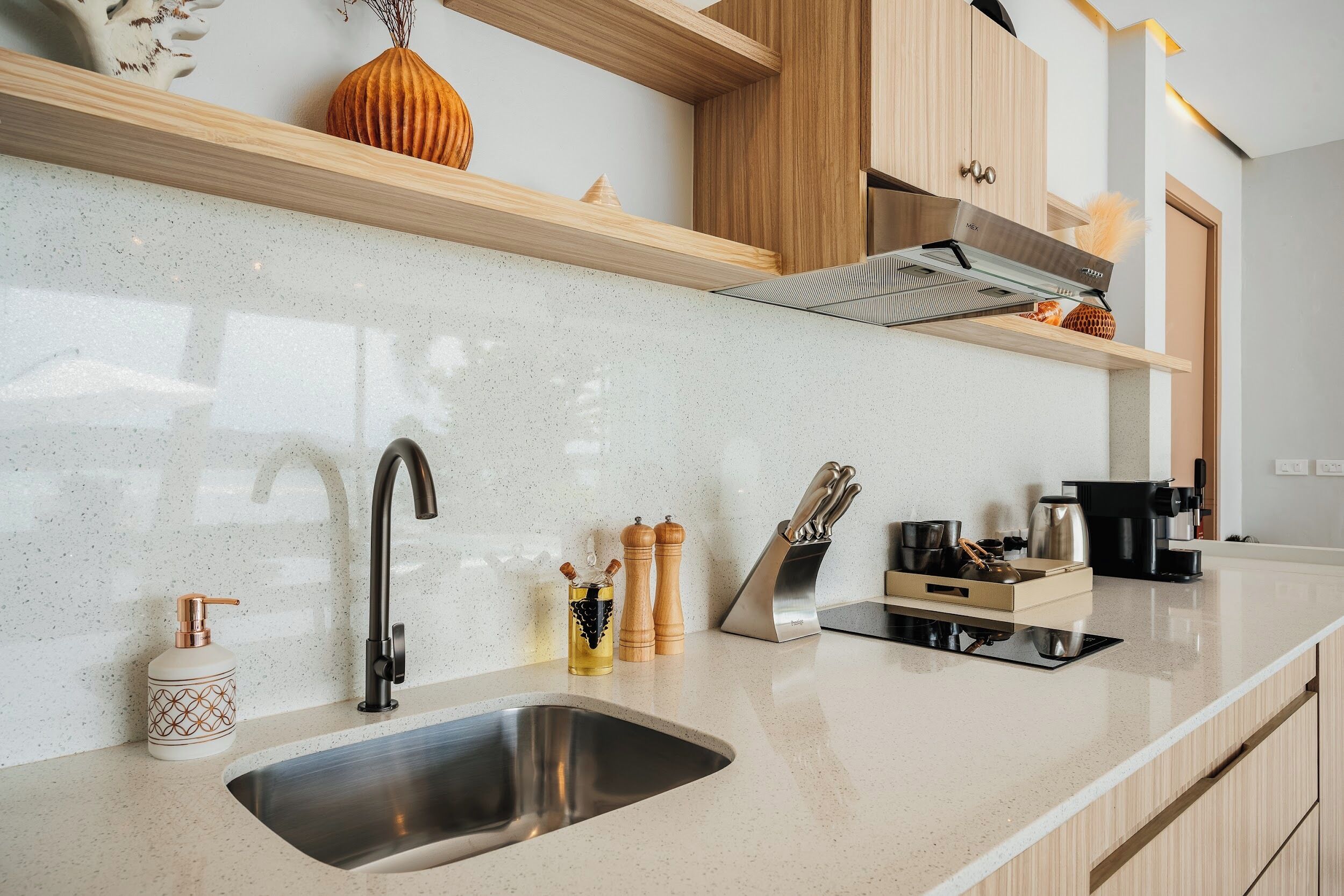Una cocina moderna con un lavamanos de acero inoxidable, armarios de madera, una campana extractora empotrada y una encimera con diversos utensilios de cocina.
