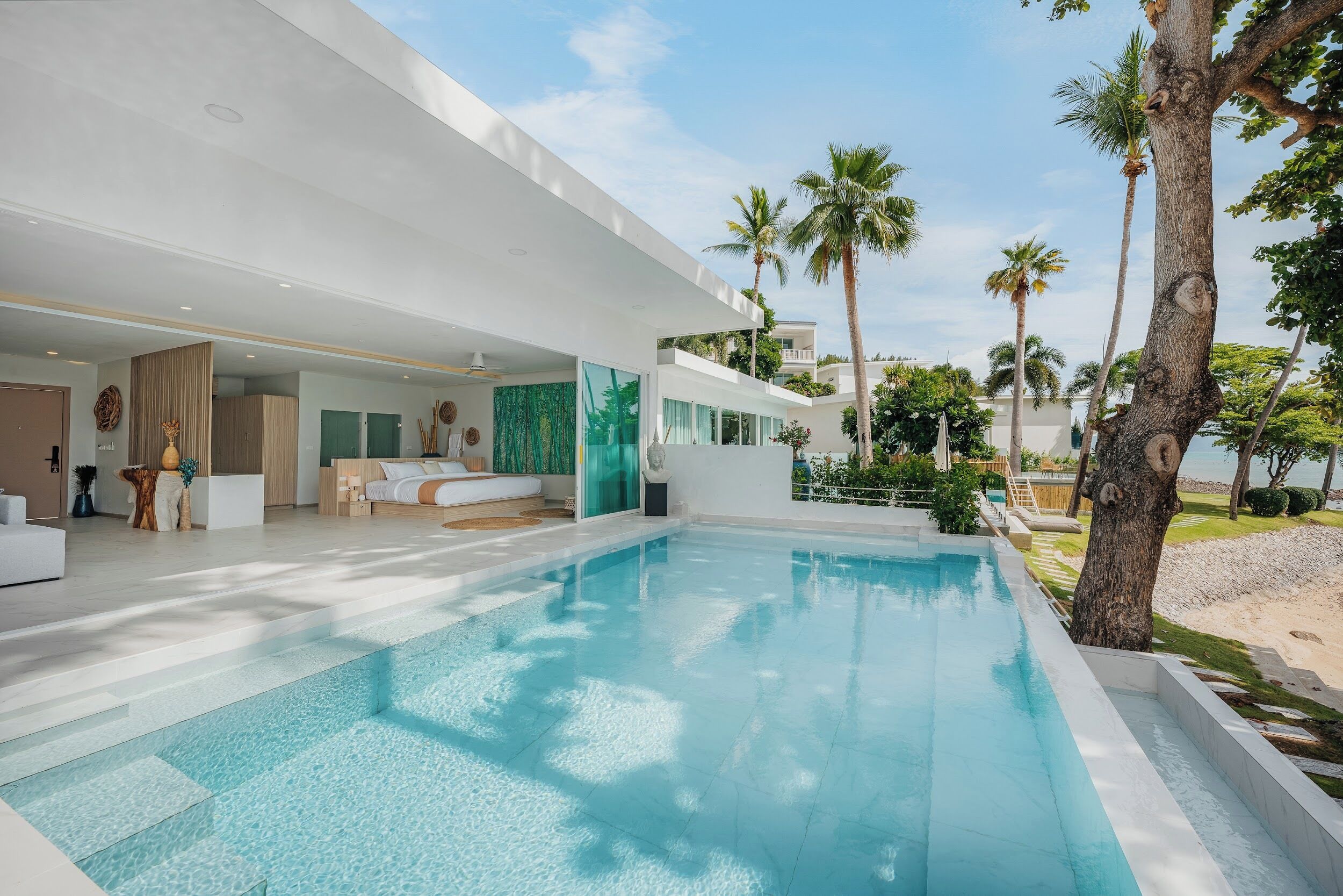 Un espace moderne aménagé au bord de la piscine, offrant une vue dégagée sur celle-ci, avec un coin salon couvert et un bâtiment doté de grandes fenêtres.