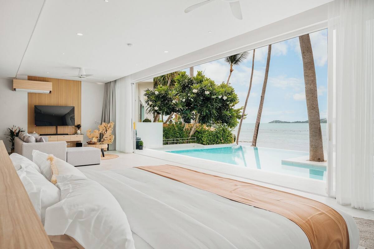 A modern bedroom with a large bed, a TV, and a view of the ocean.