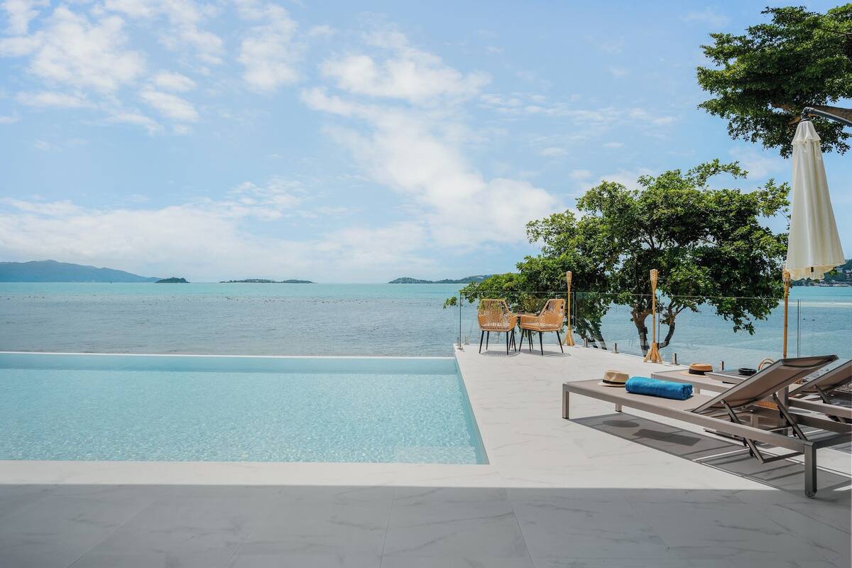 A pool with clear water, lounge chairs, and a view of the sea.