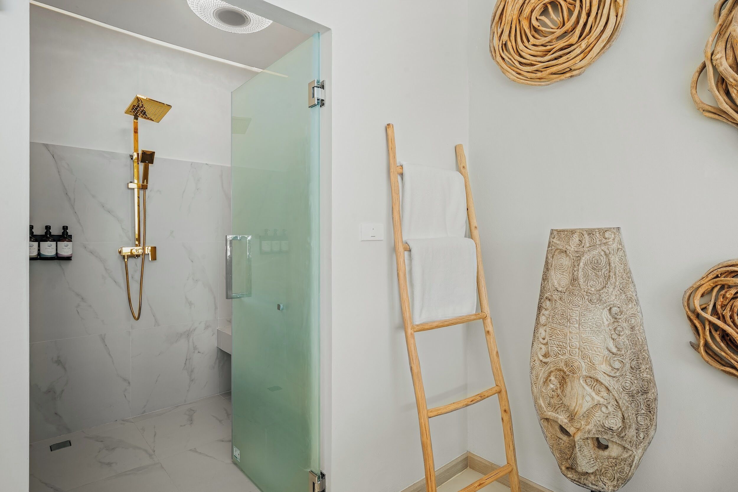 A modern bathroom with a glass shower enclosure, a wooden ladder, and a decorative wall piece.