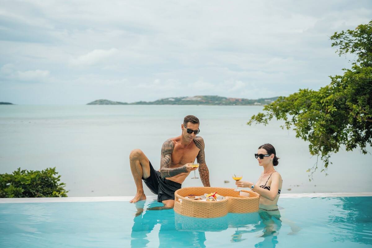 A couple relaxing by a pool with a view of the sea and distant islands.