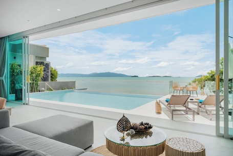 A modern poolside area with a glass balustrade, lounge chairs, and a view of the sea.
