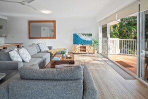 Una sala moderna con un sofá modular, un televisor de pantalla plana y un balcón con vistas a la vegetación.