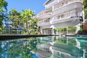 A multi-story hotel with balconies, a swimming pool, and surrounding greenery. - The Hilltop Noosa Retreat: Walk to Beach + Pool (Noosa Region)