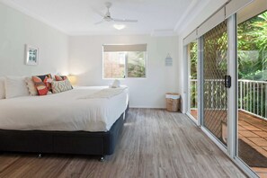 A bedroom with a bed, a ceiling fan, a window, and a sliding glass door leading to an outdoor area. - The Hilltop Noosa Retreat: Walk to Beach + Pool (Noosa Region)