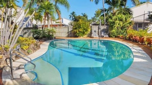 A swimming pool with a curved edge, surrounded by a wooden deck and palm trees. - Relaxed Noosaville Living - Poolside & Walkable (Noosa Region)
