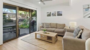 A modern living room with a sliding glass door leading to an outdoor area, a beige sofa, a wooden coffee table, and a ceiling fan. - Relaxed Noosaville Living - Poolside & Walkable (Noosa Region)