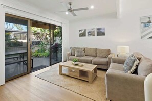 A modern living room with a sliding glass door leading to an outdoor area, a beige sofa, a wooden coffee table, and a ceiling fan. - Relaxed Noosaville Living - Poolside & Walkable (Noosa Region)