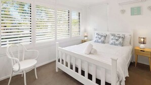 A white bedroom with a bed, two bedside tables, a chair, and a ceiling fan. - Relaxed Noosaville Living - Poolside & Walkable (Noosa Region)