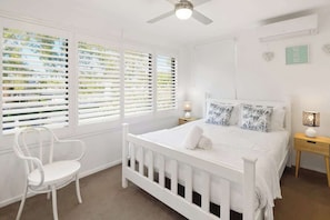 A white bedroom with a bed, two bedside tables, a chair, and a ceiling fan. - Relaxed Noosaville Living - Poolside & Walkable (Noosa Region)