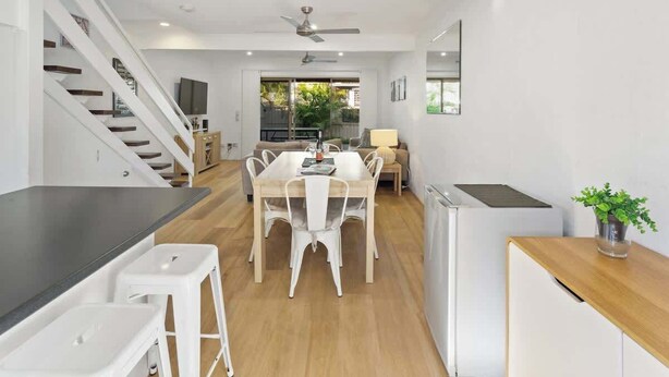 A modern kitchen with a dining area, wooden flooring, white cabinetry, and a staircase. - Relaxed Noosaville Living - Poolside & Walkable (Noosa Region)