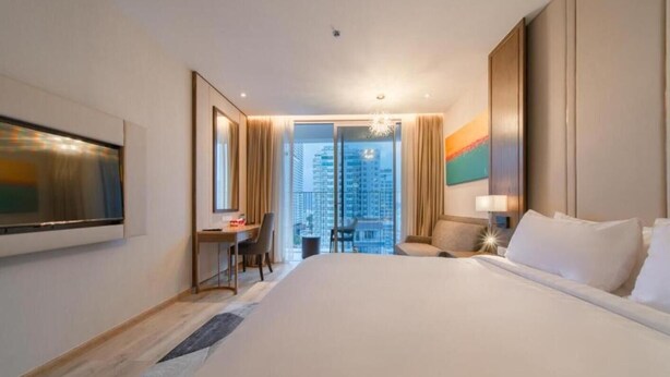 A hotel room with a large bed, a desk, a chair, a TV, and a view of the city. - Panorama Luxury Hotel - Full Services (Nha Trang)