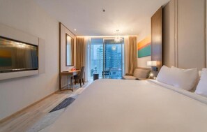 Habitación de hotel con una cama grande, un escritorio, una silla, un televisor y vistas a la ciudad.