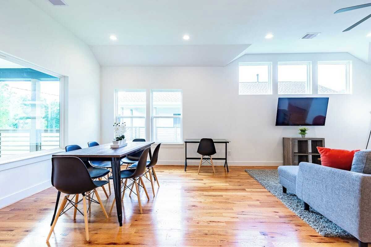 A modern living room with a dining area, large windows, and a flat-screen TV.