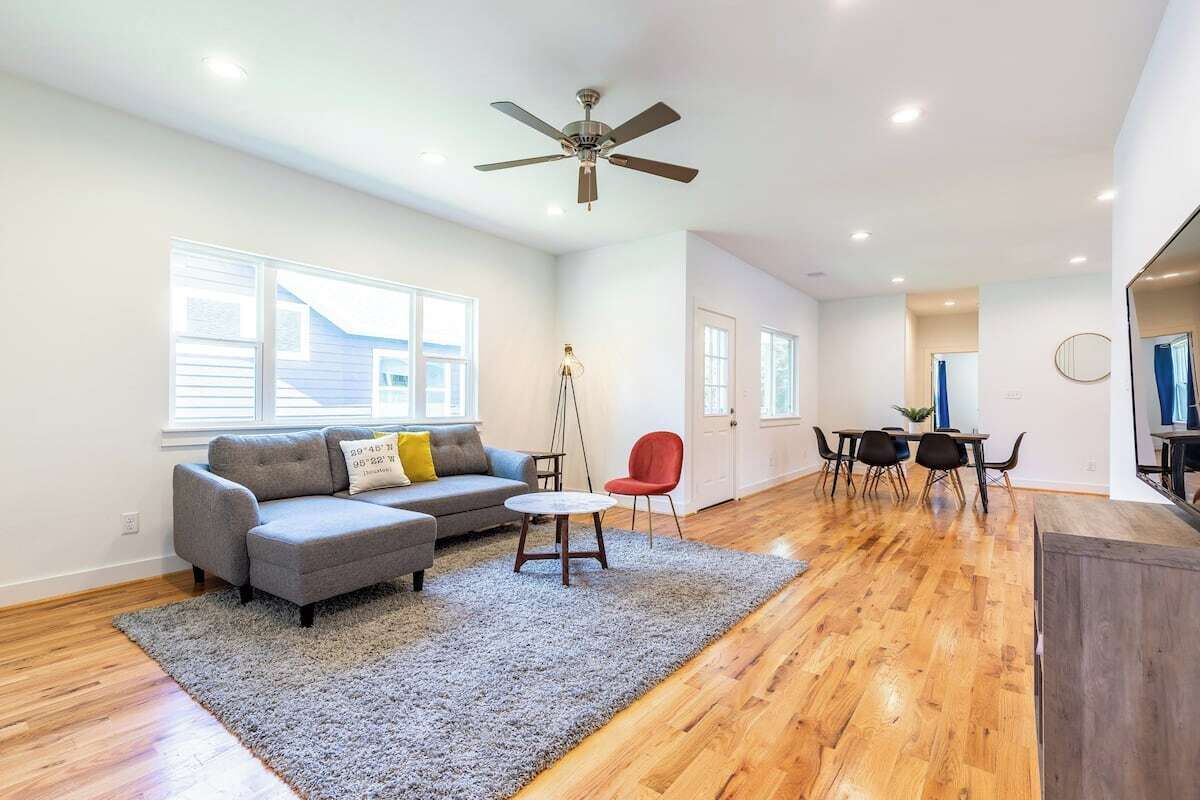 A spacious living room with a grey sectional sofa, a red chair, a small round table, and a ceiling fan.