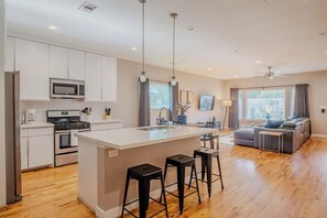 Una cocina moderna con una isla central, taburetes de bar y un rincón comedor con sofá y mesa.