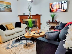 Een woonkamer met een open haard, een bank, een salontafel en een aan de muur bevestigde televisie.