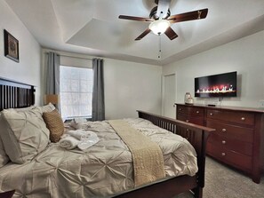 Une chambre à coucher avec un lit, un ventilateur de plafond, une télévision et une commode.
