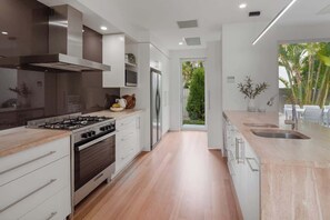 A modern kitchen with a gas stove, oven, stainless steel range hood, and a large island with a sink. - Modern Noosa River Retreat with Heated Pool (Noosa Region)