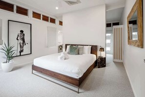 A modern bedroom with a large bed, a potted plant, a framed artwork, and a mirror on the wall. - Modern, Airy Duplex Steps to River w/ Heated Pool (Noosa Region)