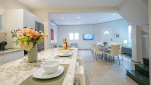 A modern kitchen with a marble countertop, a dining area with a TV, and a living space with a TV.